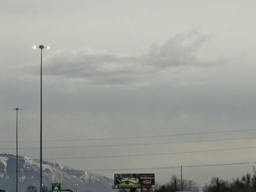 Clouds in the sky resembling a submarine, with a lamppost and snowy mountains in the background.