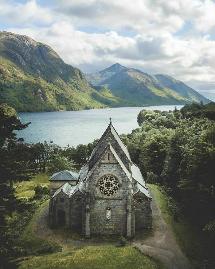 A historic church by a lake with mountains in the background, showcasing fascinating architecture and tranquil scenery.