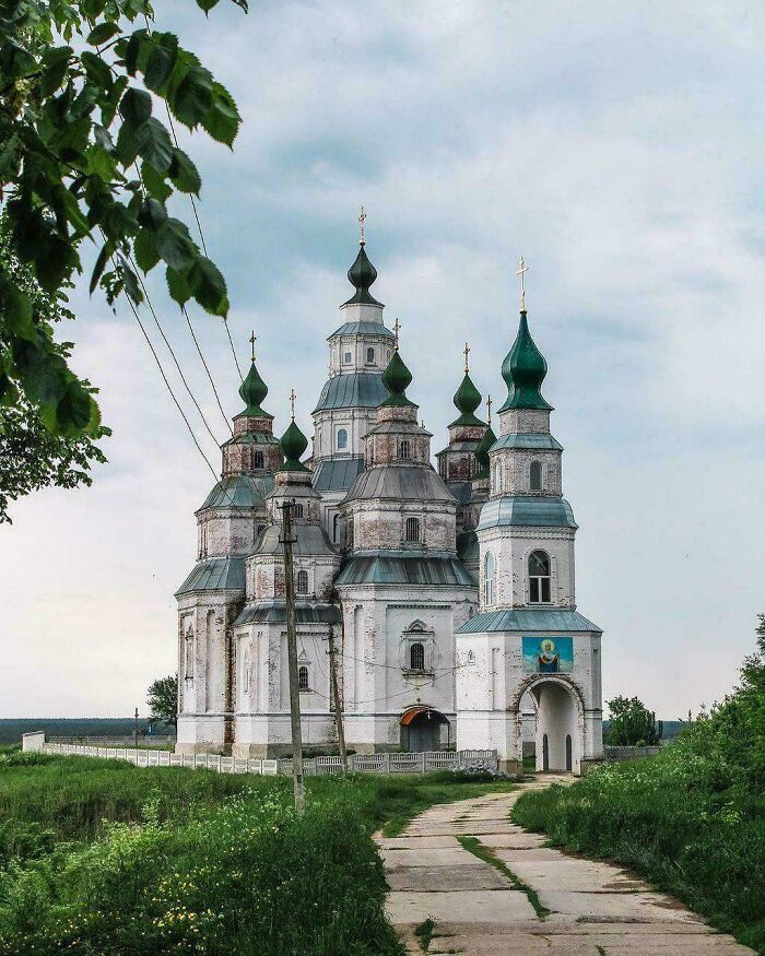 Historic church with green domes surrounded by greenery, showcasing fascinating architecture against a cloudy sky.