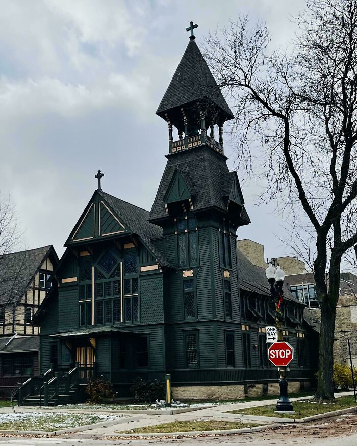 Historic church with Gothic architecture, dark wood exterior, and tall spire, captured on an overcast day.