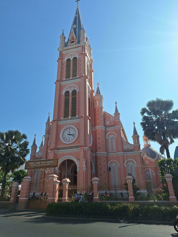 Pink Gothic-style church with tall spire against a clear blue sky, showcasing fascinating architecture.