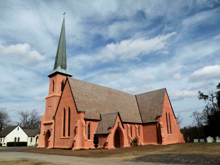 A captivating photo of a red brick church with a tall spire against a blue sky.