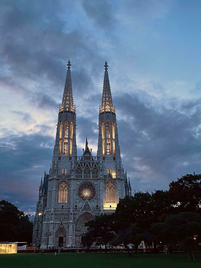 Illuminated church with twin spires against a dramatic evening sky, showcasing fascinating architectural details.