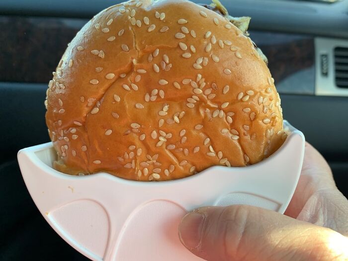 Burger in a white holder to minimize mess, showcasing innovative Less-Mess-2025 solution in a car setting.