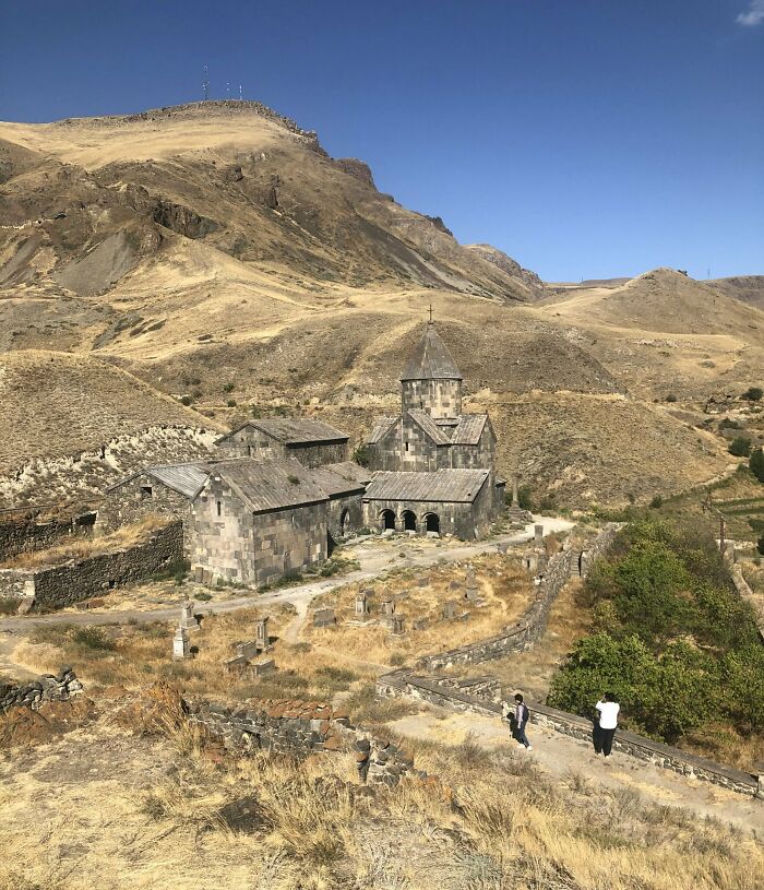 Ancient stone church nestled in a rugged, mountainous landscape under a clear blue sky, showcasing fascinating church architecture.