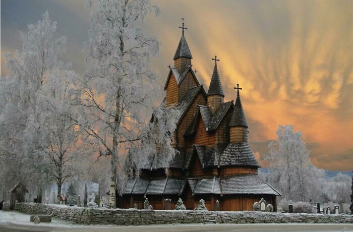 Snow-covered wooden church with tall spires under a vibrant, colorful sky; a captivating scene.