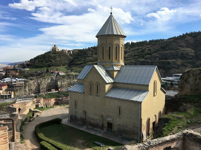 Fascinating church with a tall steeple set against a scenic hilly landscape under a partly cloudy sky.