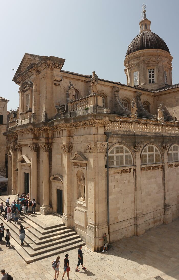 Historic church with intricate architecture, stone carvings, and a domed roof. Visitors gather at the entrance.