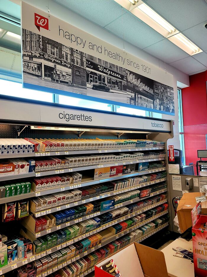 Cigarette display at a local pharmacy, with a vintage Walgreens sign above, highlighting a contradiction in health branding.