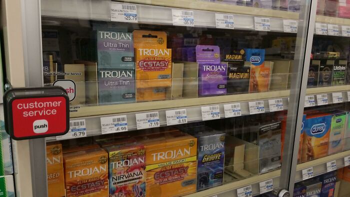 A locked pharmacy shelf displaying various condom brands, with a customer service button nearby.