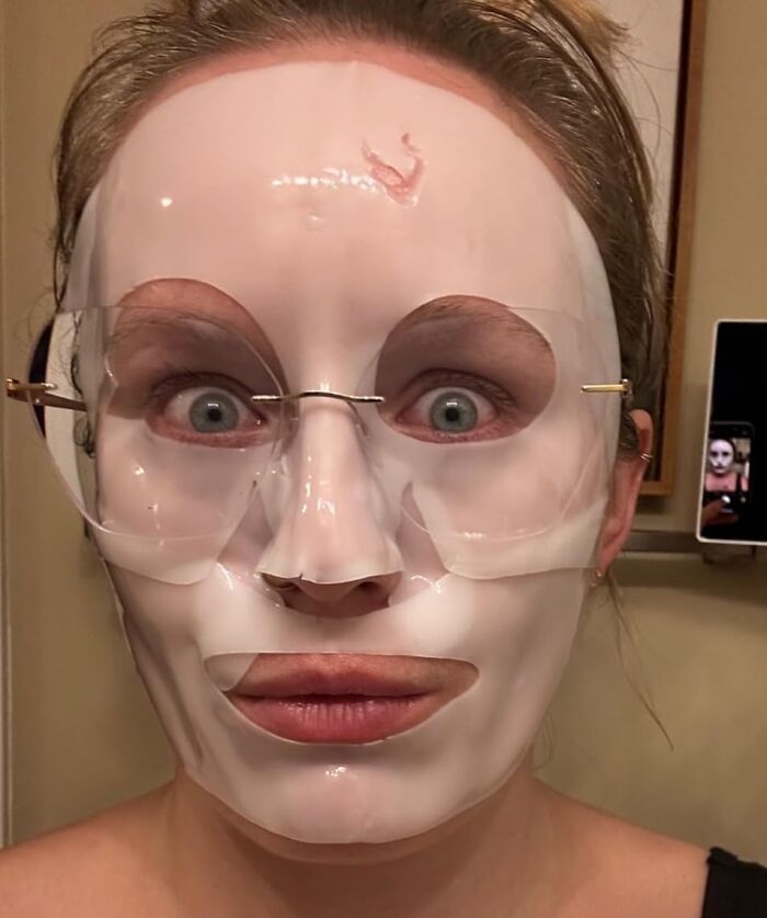 Person wearing a hydrating face mask and glasses, enjoying cozy products indoors.