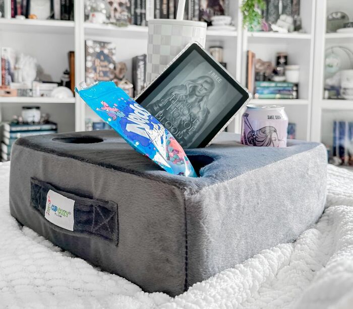 Cozy products for relaxing indoors: a lap desk with snacks, a drink, and an e-reader on a fluffy blanket.