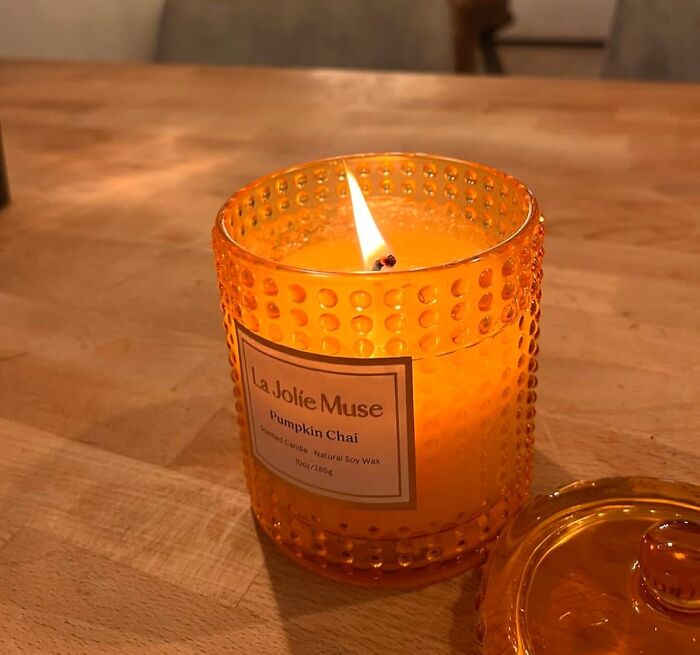 Orange pumpkin chai candle burning on a wooden table, ideal cozy product for relaxing indoors.