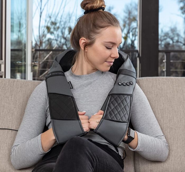 Woman relaxing on a couch using a neck massager, a cozy product for doing nothing inside.