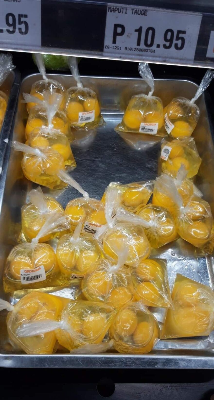 Plastic bags of oranges on display, highlighting wasteful unnecessary packaging in a grocery store setting.