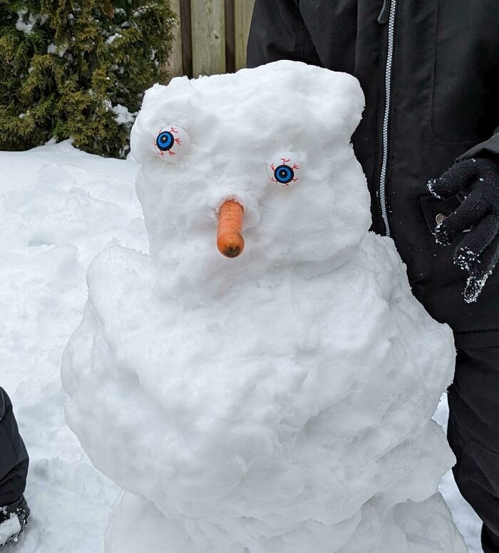 Snowman with a carrot nose and funny eyes, created by children in winter, showcasing hilarious kids' creativity.