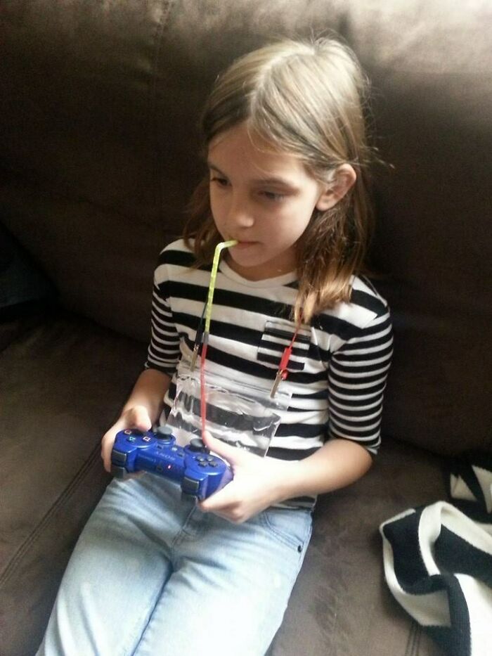 Child humorously drinks with straw, holding a game controller, embodying hilarious-kids theme.