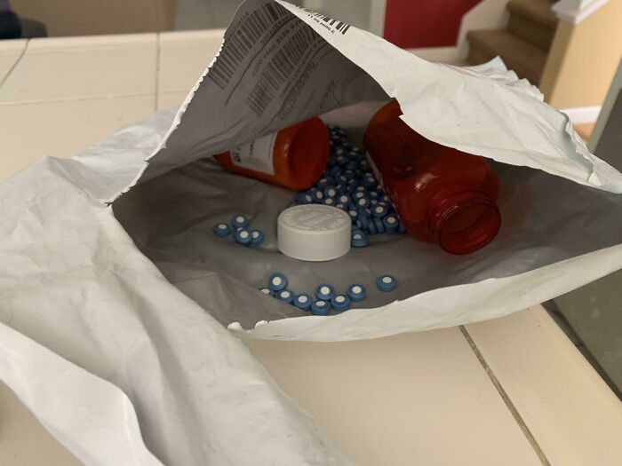 Open package with spilled pills and caps from local pharmacies on a countertop.