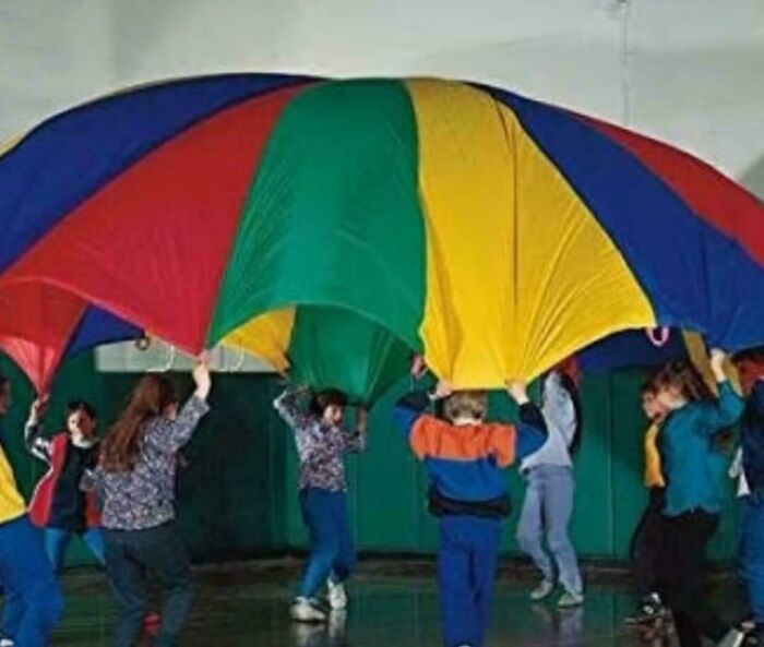 Kids playing with a colorful parachute indoors, evoking 80s nostalgia.