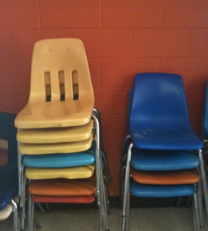 Stack of colorful plastic chairs against an orange brick wall, evoking 80s nostalgia.