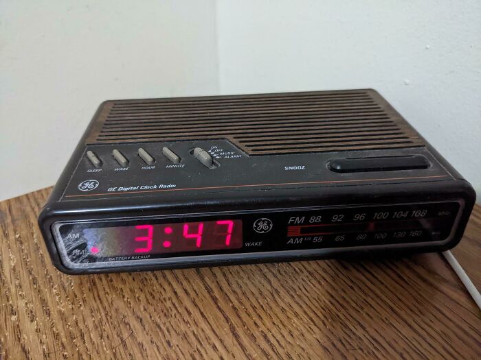 80s nostalgia: A vintage digital clock radio displaying the time 3:47, sits on a wooden surface.