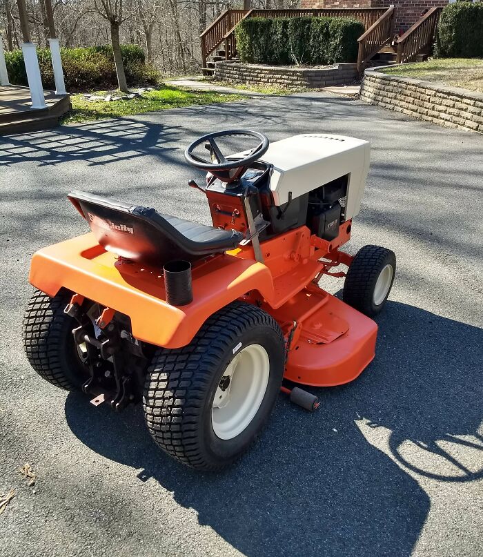 Vintage 80s lawn tractor with an orange body parked on a driveway, evoking nostalgia.