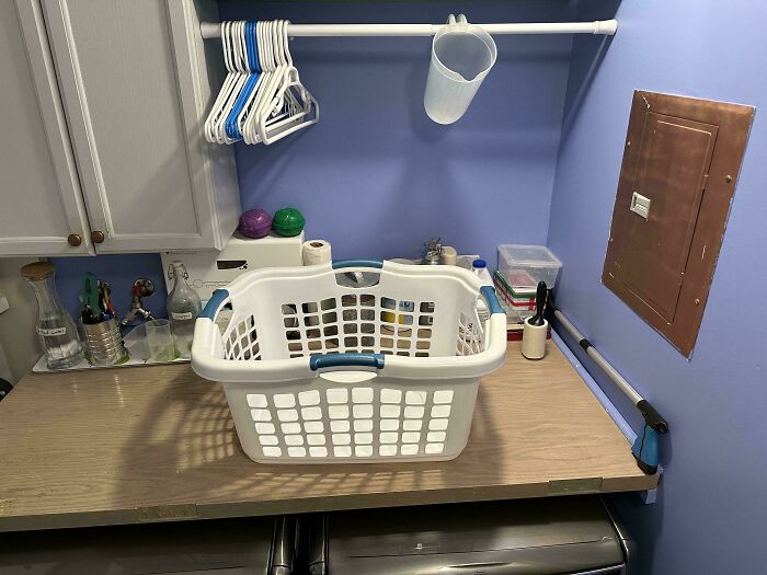 Laundry room with 80s nostalgia elements: white basket, wire hangers, and wooden table for folding.