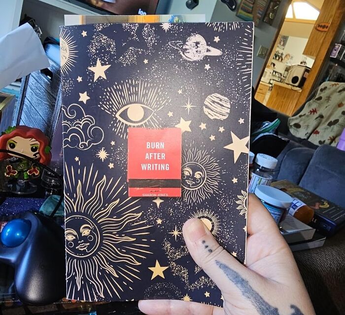 A hand holding a celestial-themed journal titled "Burn After Writing," a perfect treasure to reward yourself after a busy day.