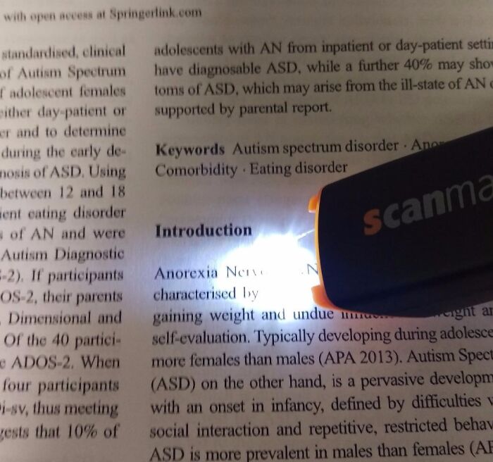 Portable scanner highlighting text on a page, showcasing innovative gadget use.