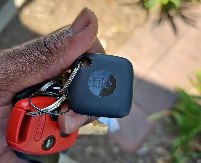 Hand holding keys with a Tile tracker, one of the best gadgets for 2025, against a blurred outdoor background.