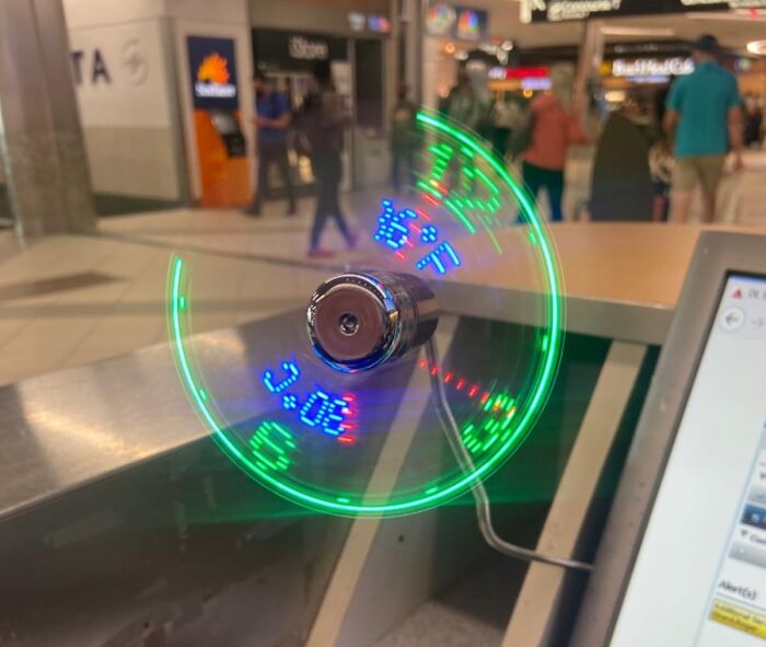 Innovative gadget displaying time and temperature with LED lights in a busy shopping center, highlighting future tech trends.