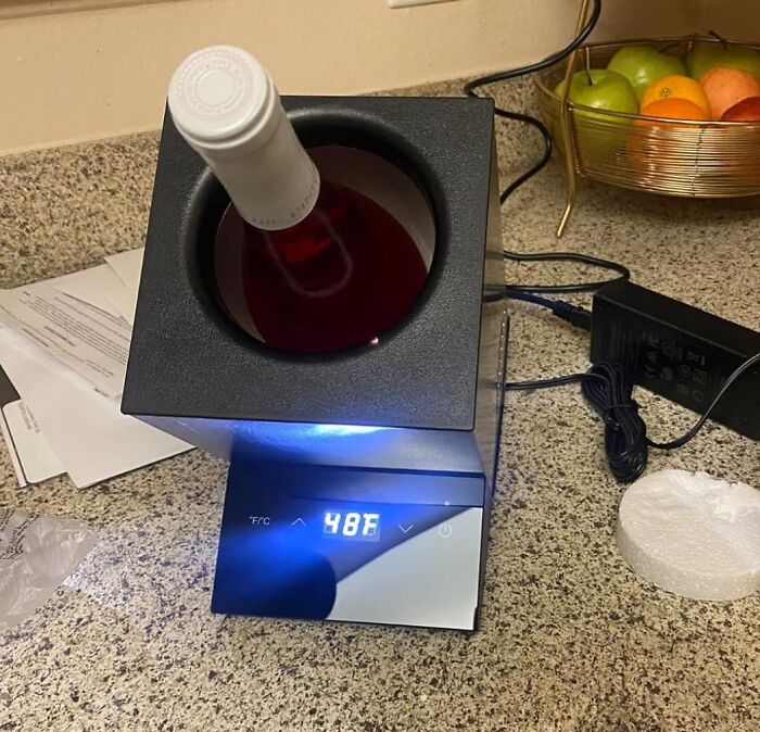 A wine bottle chiller gadget on a countertop displaying a temperature of 48°F, next to a fruit basket.