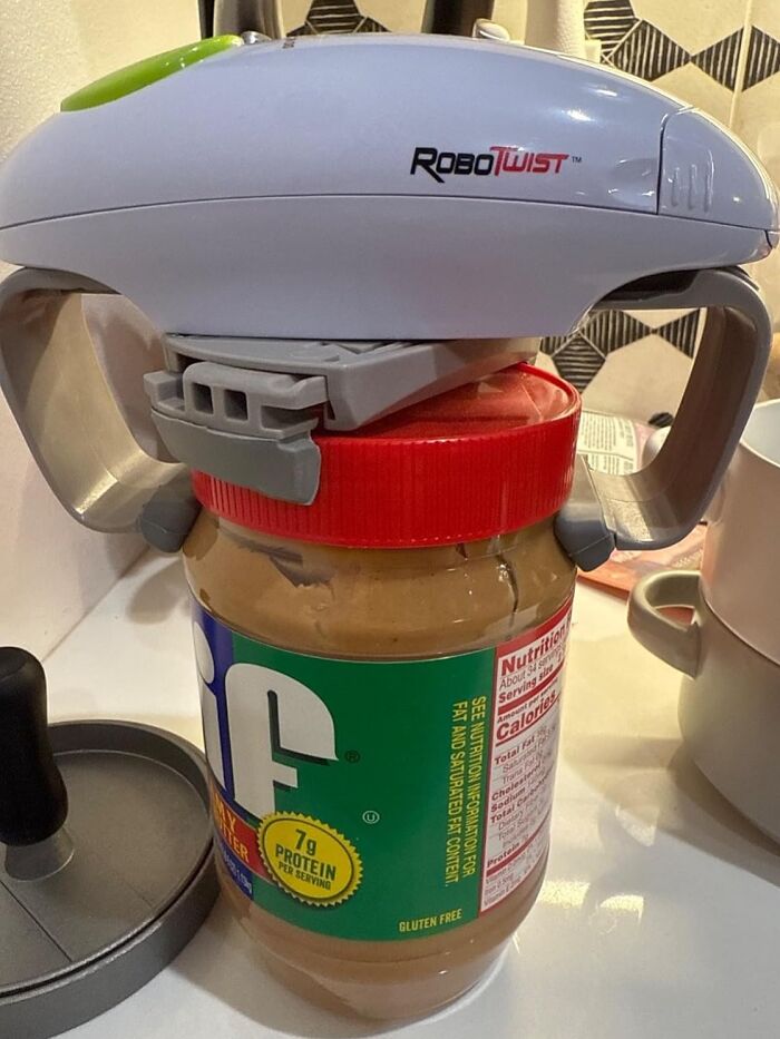 Robotic jar opener gadget on a peanut butter jar in a kitchen setting.