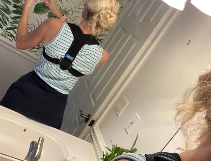 Woman in a striped tank top using a back posture corrector in a bathroom for a more responsible lifestyle.