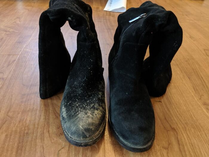 Worn black boots on a wooden floor, one dirty, emphasizing responsible care for personal items.