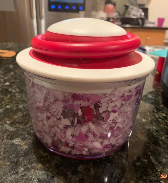 Chopped onions in a manual food processor on a kitchen counter, promoting responsible cooking habits.