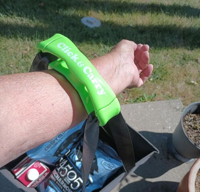 A hand using a green Click & Carry handle, demonstrating a responsible way to carry multiple grocery bags outdoors.