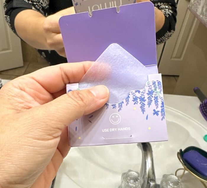 Hand holding purple sachet labeled "Use Dry Hands" near a bathroom sink, reflecting responsible habits.