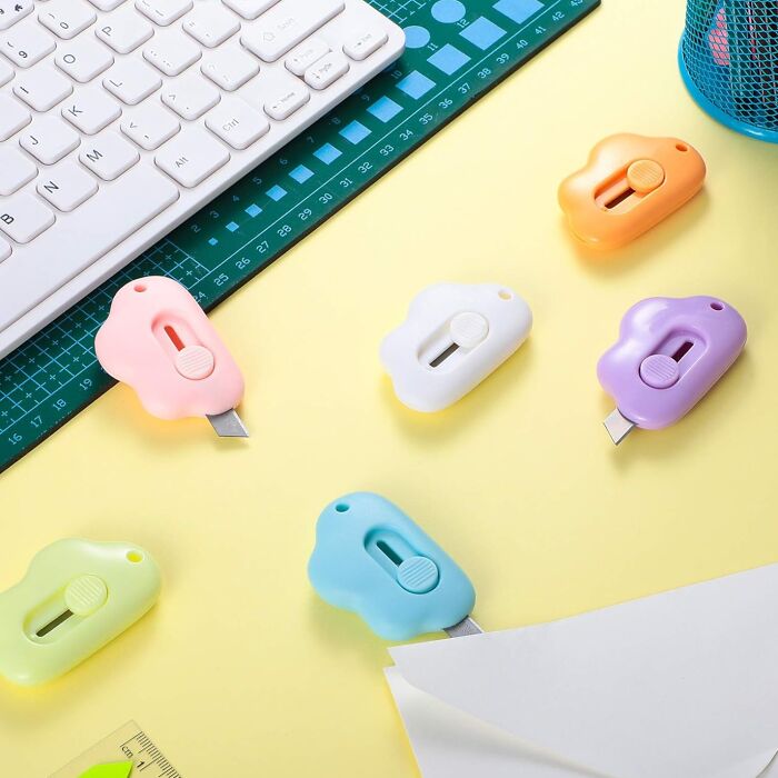 Colorful cloud-shaped box cutters and a keyboard on a desk, showcasing fun office supplies.