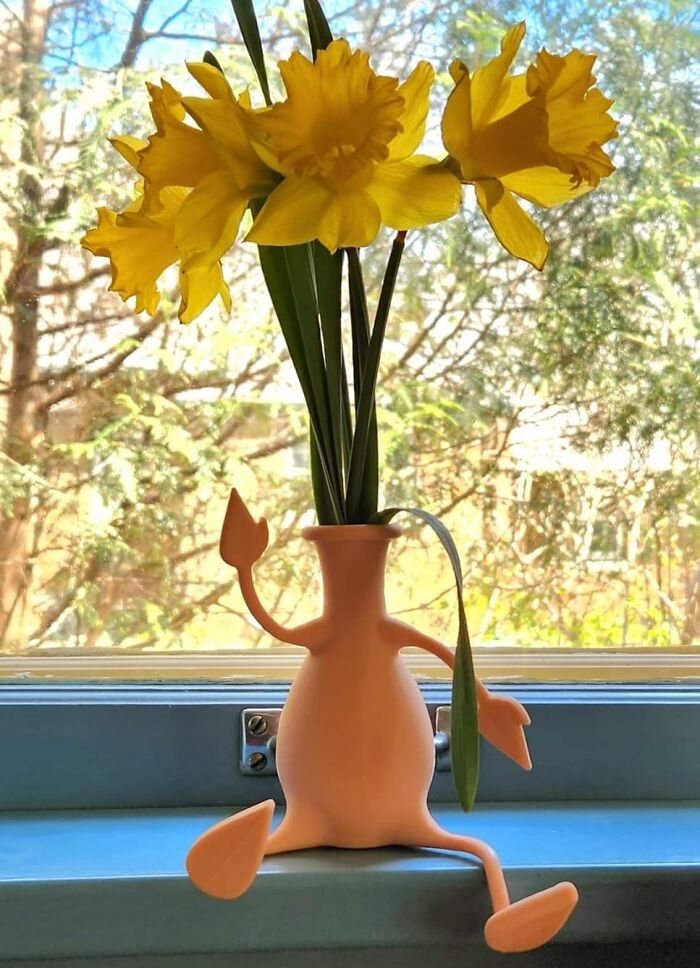 Fun office supplies: quirky vase shaped like a character, holding yellow daffodils, placed on a windowsill.