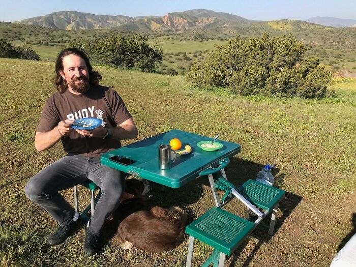 Man enjoying a picnic at a green table with scenic hills, evoking 80s nostalgia.