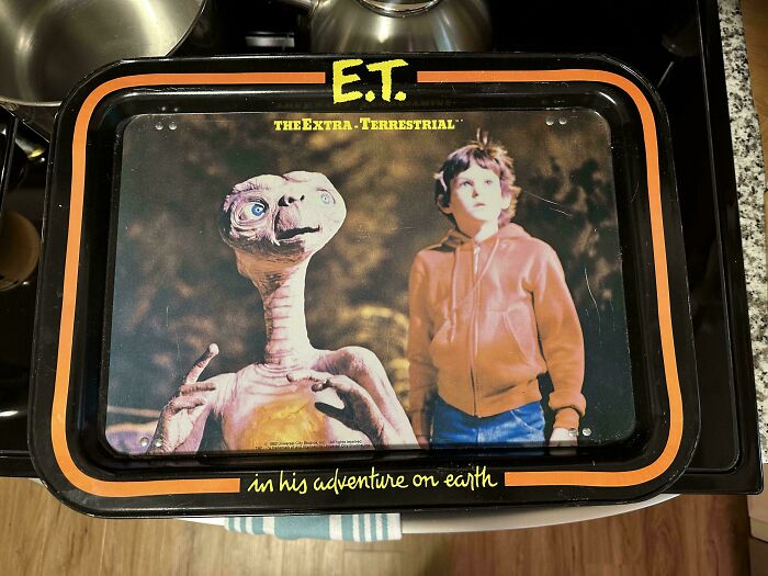 80s nostalgia picture of E.T. and a boy in an orange hoodie from "E.T. the Extra-Terrestrial" on a metal tray.