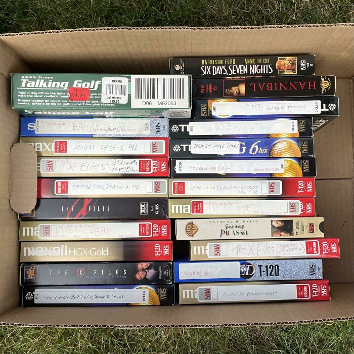 Box of VHS tapes featuring 80s nostalgia, including popular movies and TV shows.