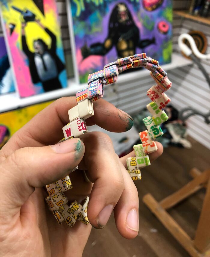 Hand holding a 1980s nostalgia-inspired origami bracelet, with vibrant pop art paintings in the background.