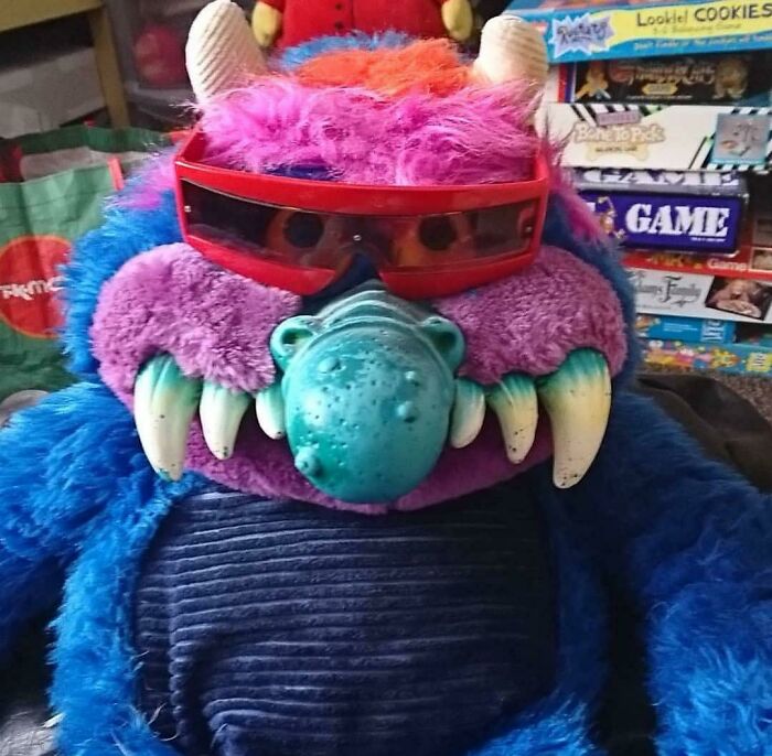 1980s nostalgia with a colorful plush monster toy wearing sunglasses, surrounded by retro board games.