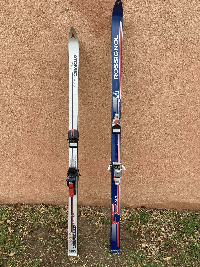 80s nostalgia skis, Atomic and Rossignol, leaning against a wall with grass below.