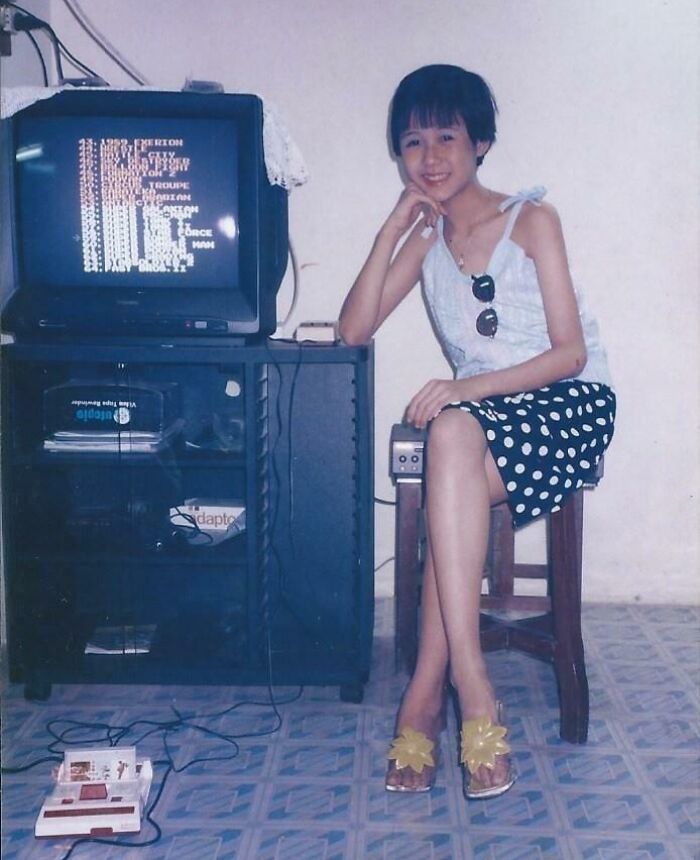 Young woman in 80s fashion sitting next to a vintage TV and gaming console, capturing 80s nostalgia.