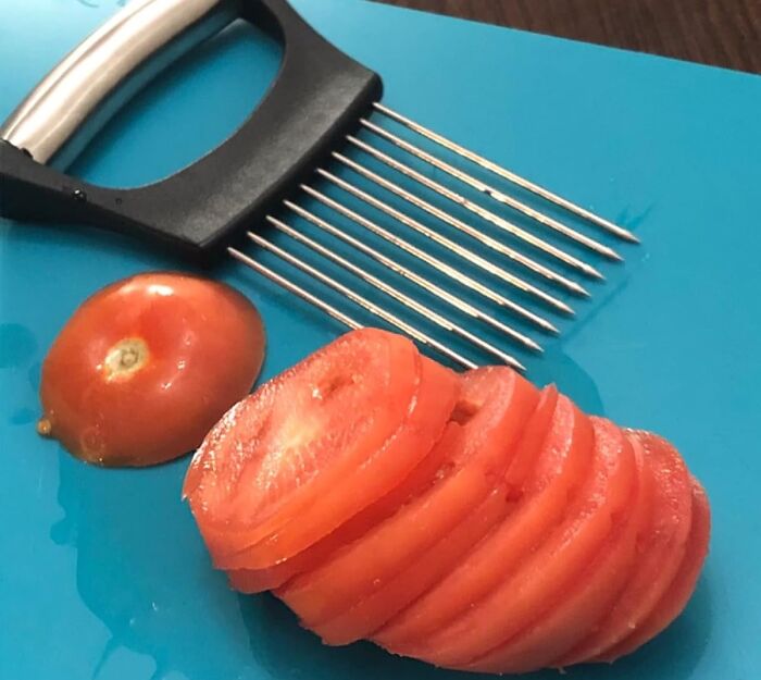 Sliced tomato next to a slicing tool on a blue cutting board, illustrating a step to get better at cooking.