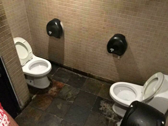 Dos inodoros mal instalados en baño público, mostrando empleados perezosos en construcción.