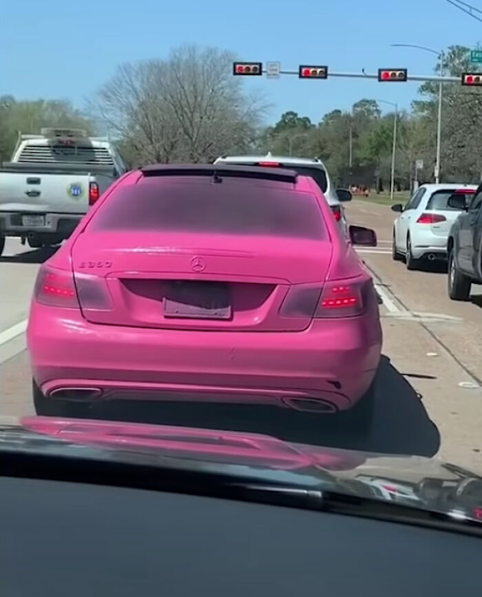 Coche rosa con matrícula difuminada en un semáforo, ejemplo de empleados perezosos.